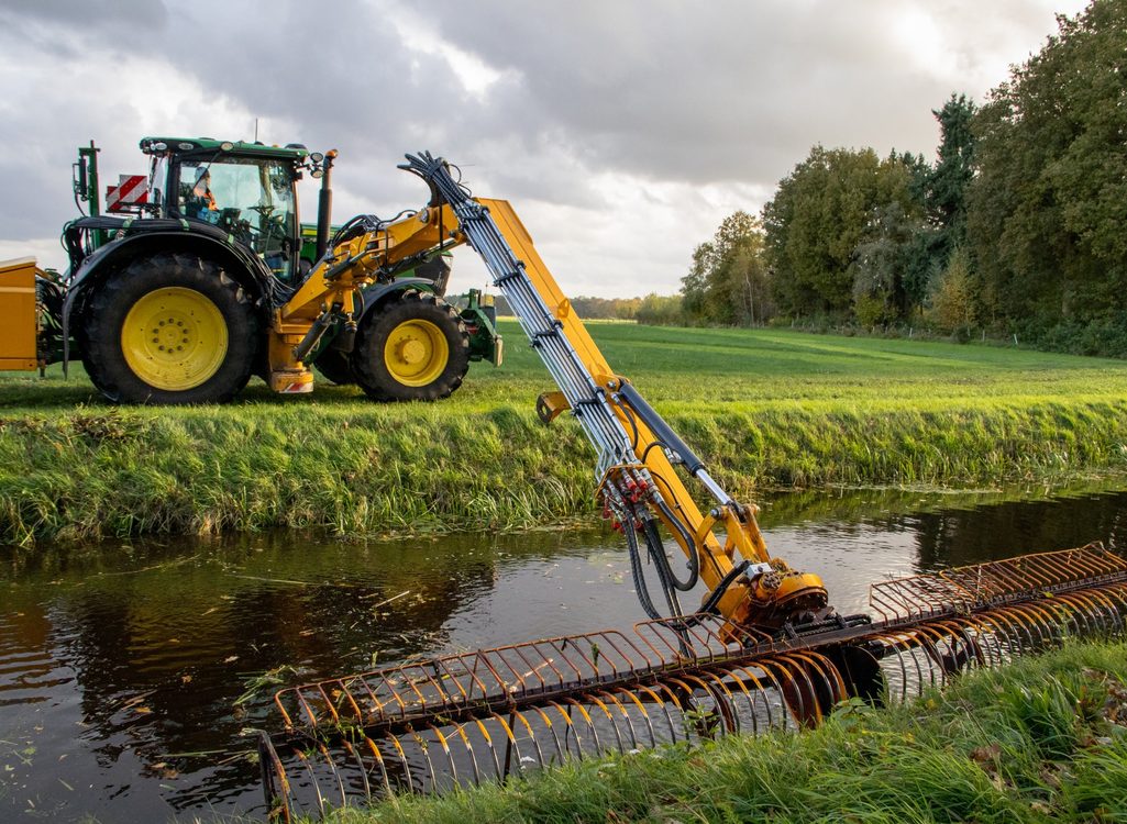 Tractor met maaiarm maait een sloot langs een weiland
